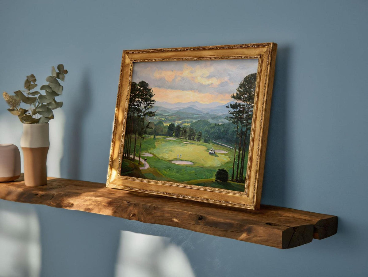 a wooden shelf displaying a framed landscape painting depicting a serene golf course surrounded by trees and mountains.