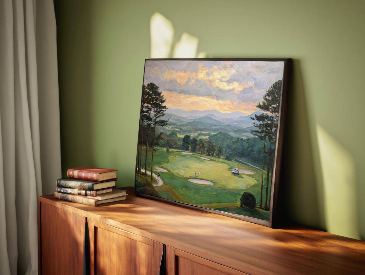 a framed painting of a golf course with a scenic landscape in the background, placed on a wooden cabinet or shelf.