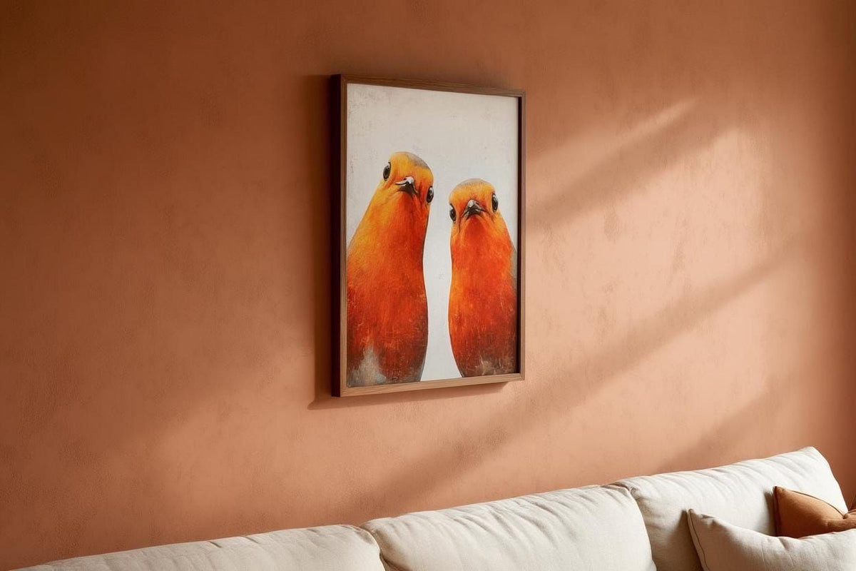 two birds, possibly a pair of parrots, in a framed artwork hanging on a peach-colored wall above a white couch.
