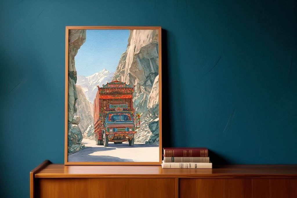 A framed painting depicting a colorful truck driving through a mountainous landscape is displayed on a wooden shelf against a blue wall.