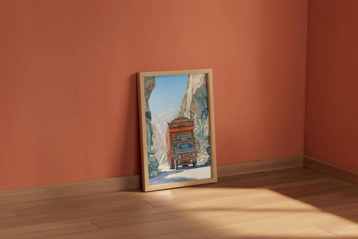 a framed painting of a red truck driving through a snowy mountain landscape, set against a peach-colored wall.