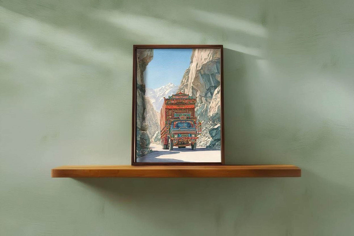 A framed photograph of a colorful truck driving through a mountainous landscape is displayed on a wooden shelf against a green wall.