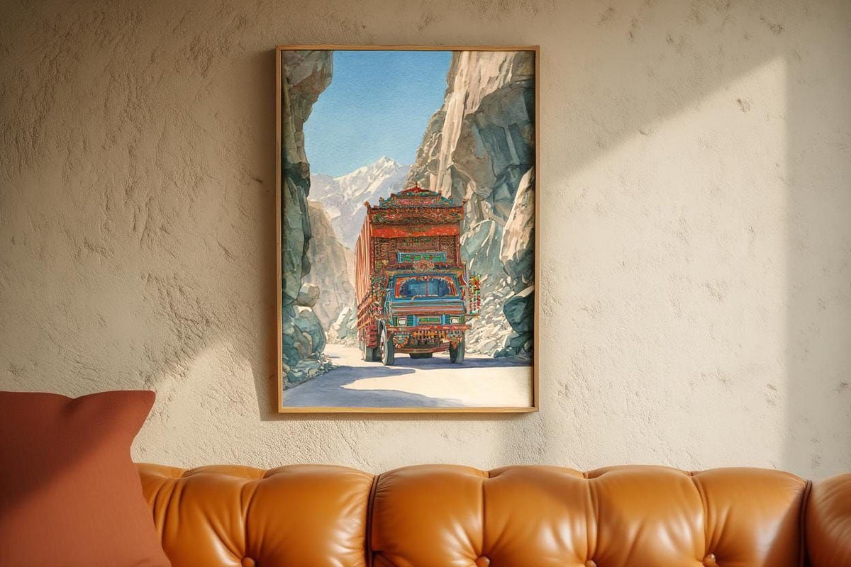A framed painting of a colorful truck driving through a mountainous landscape is hanging on a wall above a brown leather couch.