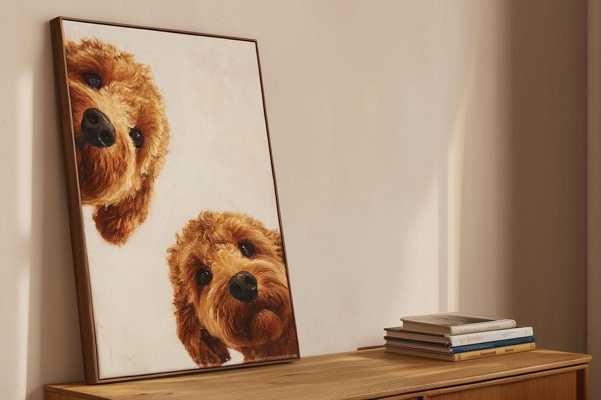 two brown poodles peeking out from behind a framed painting on a wooden surface.