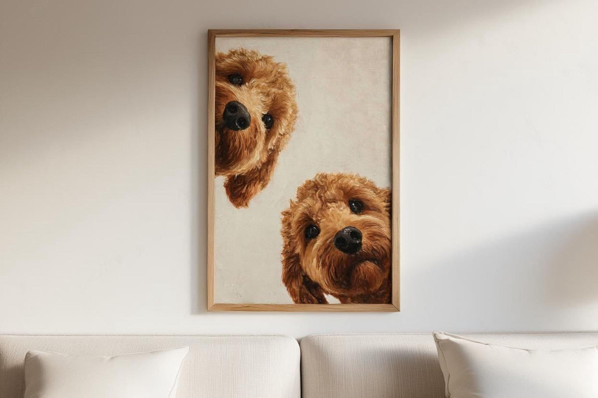 two brown dogs peeking out from behind a wooden frame, which is hanging on a white wall above a couch.