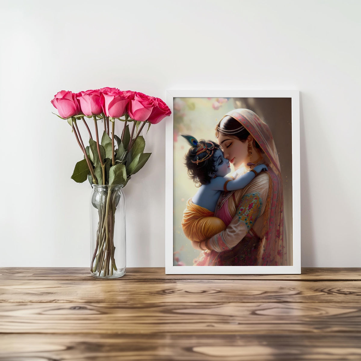 a framed painting of a woman holding a child, with a vase of pink roses on a wooden surface next to the frame.