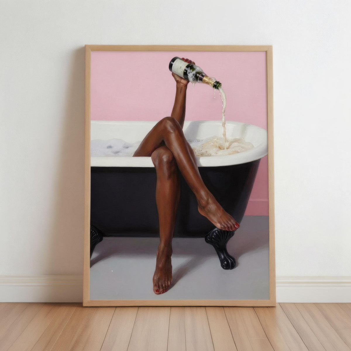 Framed print leaning on wooden floor, black woman bathroom wall art, legs crossed pouring champagne into clawfoot tub