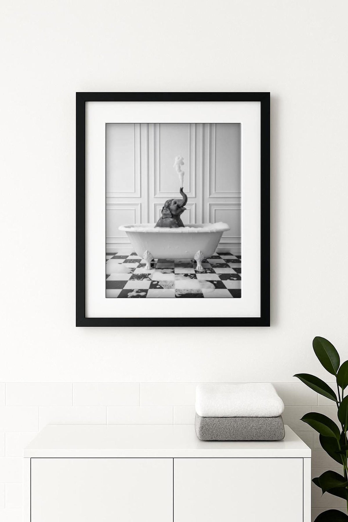 A framed black and white photograph of a baby elephant sitting in a bathtub, with steam rising from the tub.