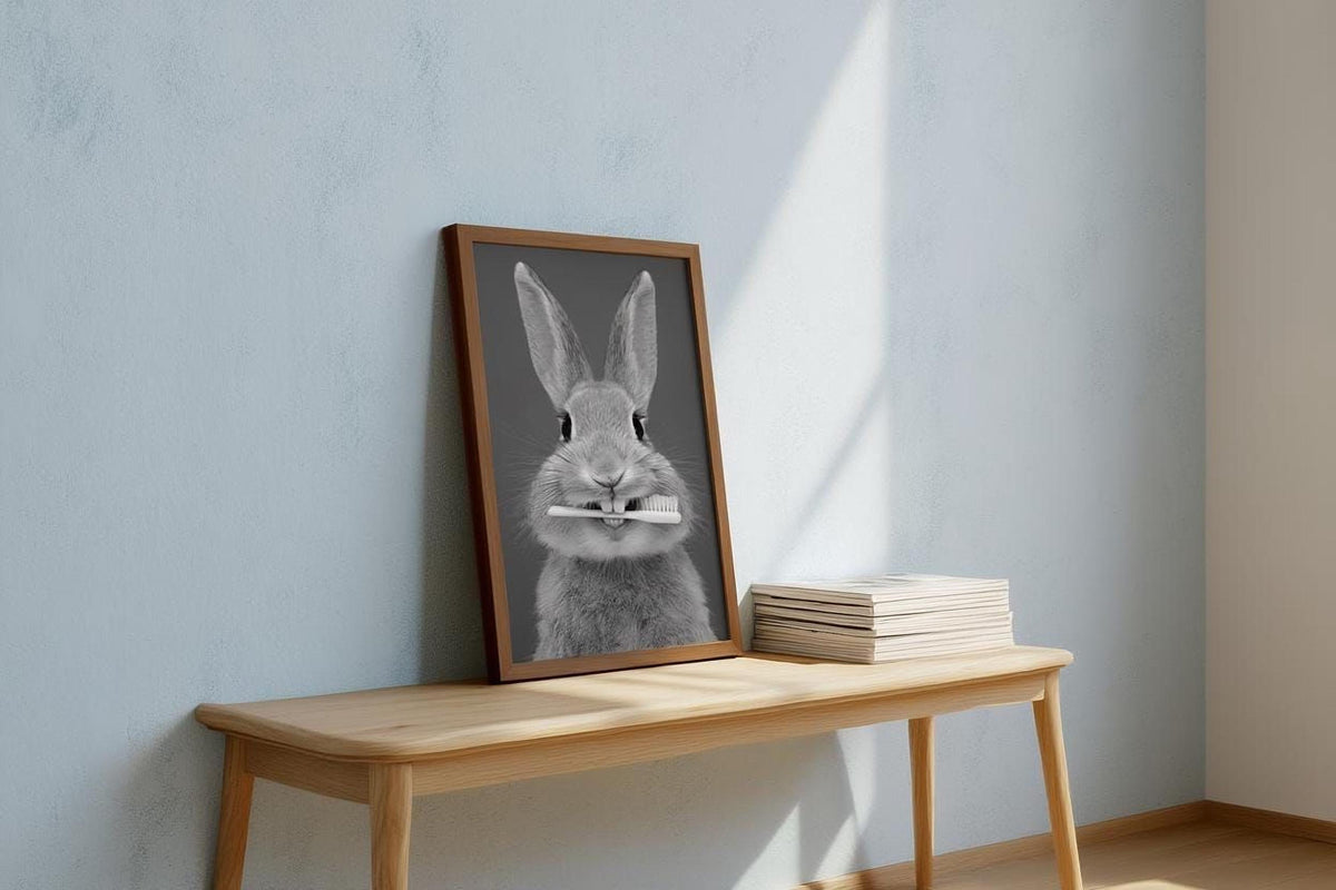 A framed image of a rabbit holding a toothbrush is displayed on a wooden table, with a stack of books and a light blue wall in the background.