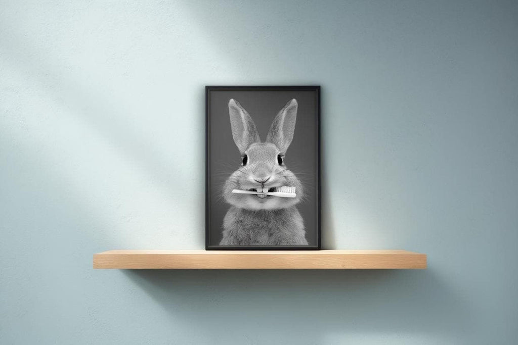 A black and white photograph of a rabbit holding a toothbrush in its mouth, placed on a wooden shelf against a light blue wall.
