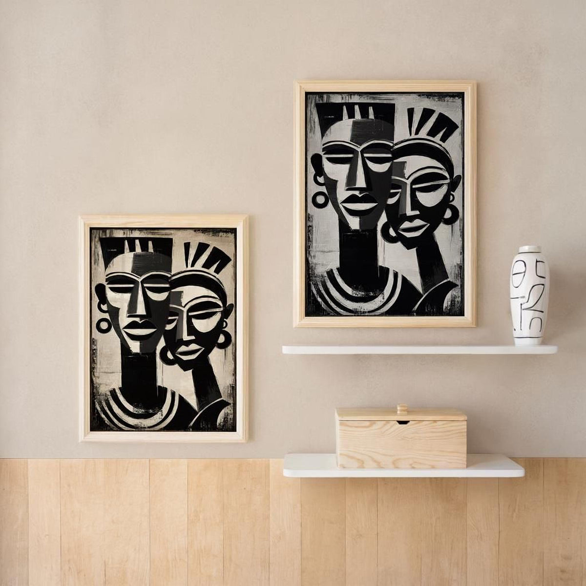 two framed black and white portraits of stylized human faces, hanging on a wall above a wooden shelf.
