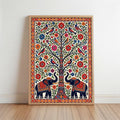 The image is a framed artwork depicting a tree with various colorful flowers and birds, including two elephants. The elephants are adorned with intricate patterns and designs, adding to the overall visual appeal of the scene.