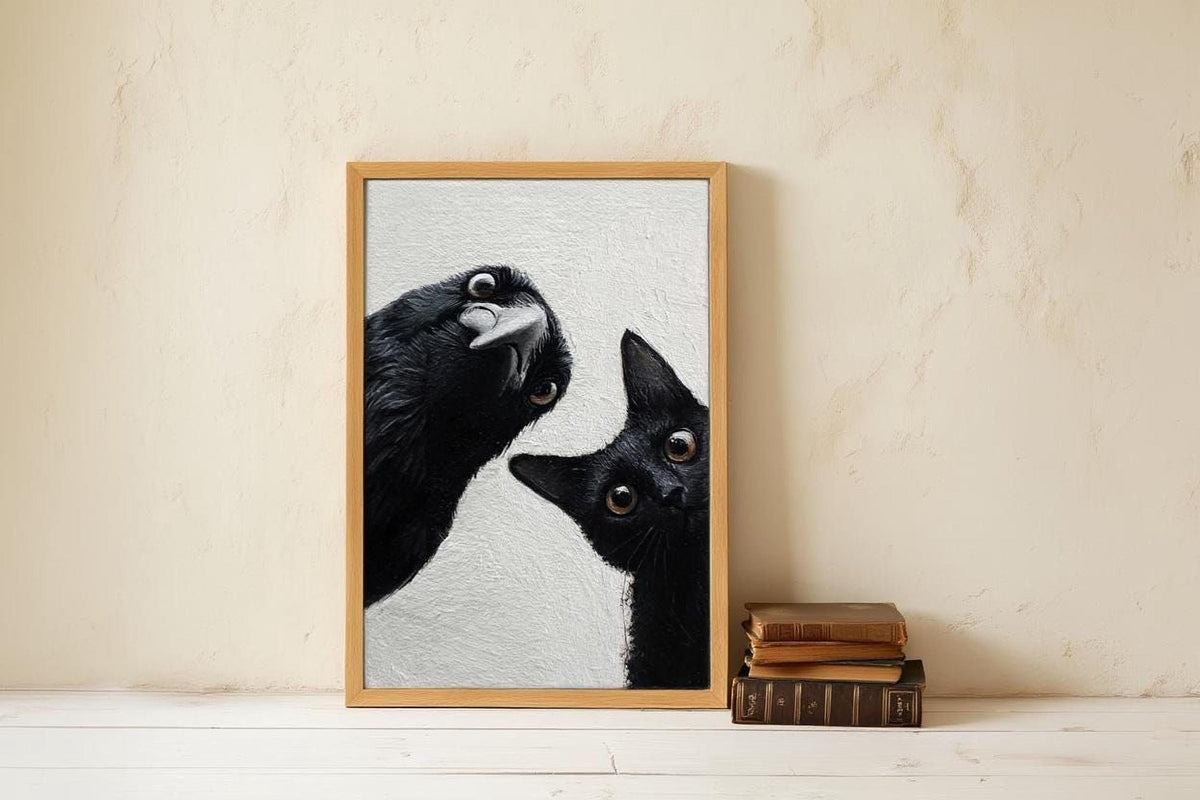 A framed photograph of a black cat peeking out from behind a black bird, with a stack of books next to it on a white wall.