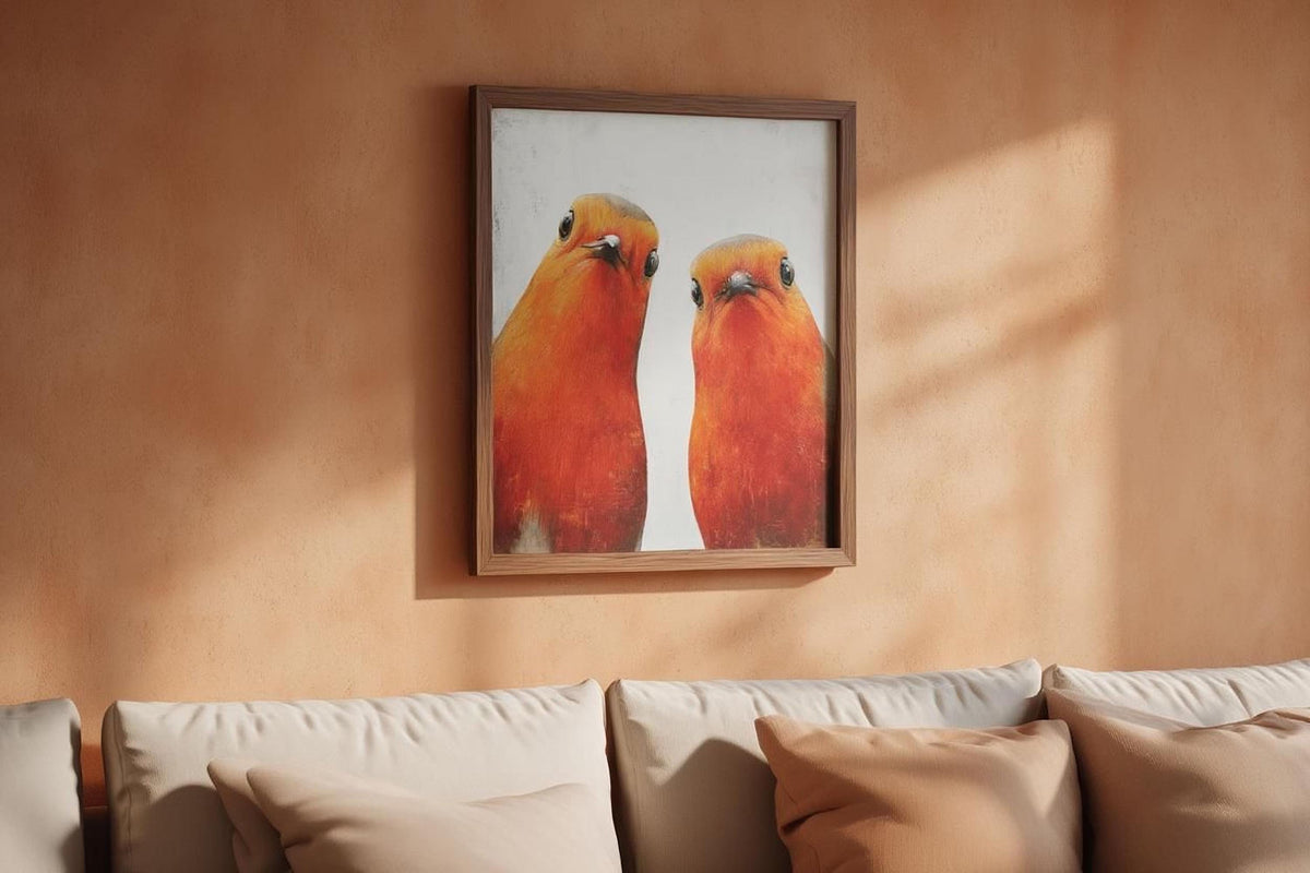 a framed painting of two birds, likely a parrot, hanging on a peach-colored wall above a beige couch with pillows.
