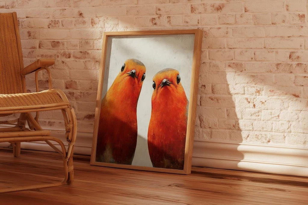 two vibrant orange birds standing side by side, with their heads turned towards the camera. The birds are positioned in the center of the frame, creating a striking visual contrast against the white background. The wooden floor and white brick wall provide a warm and natural backdrop for the scene.