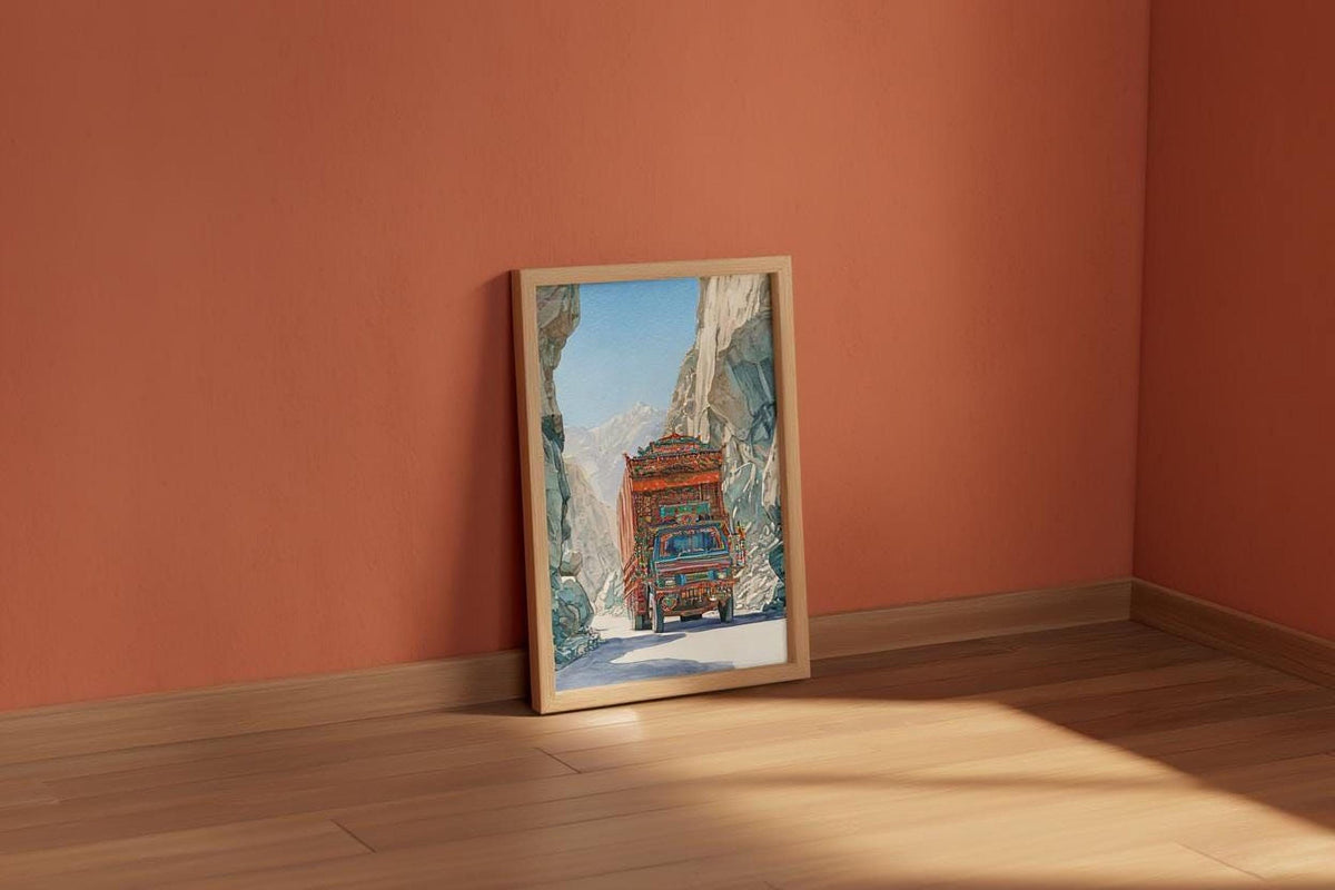 a framed painting of a red truck driving through a snowy mountain landscape, set against a peach-colored wall.