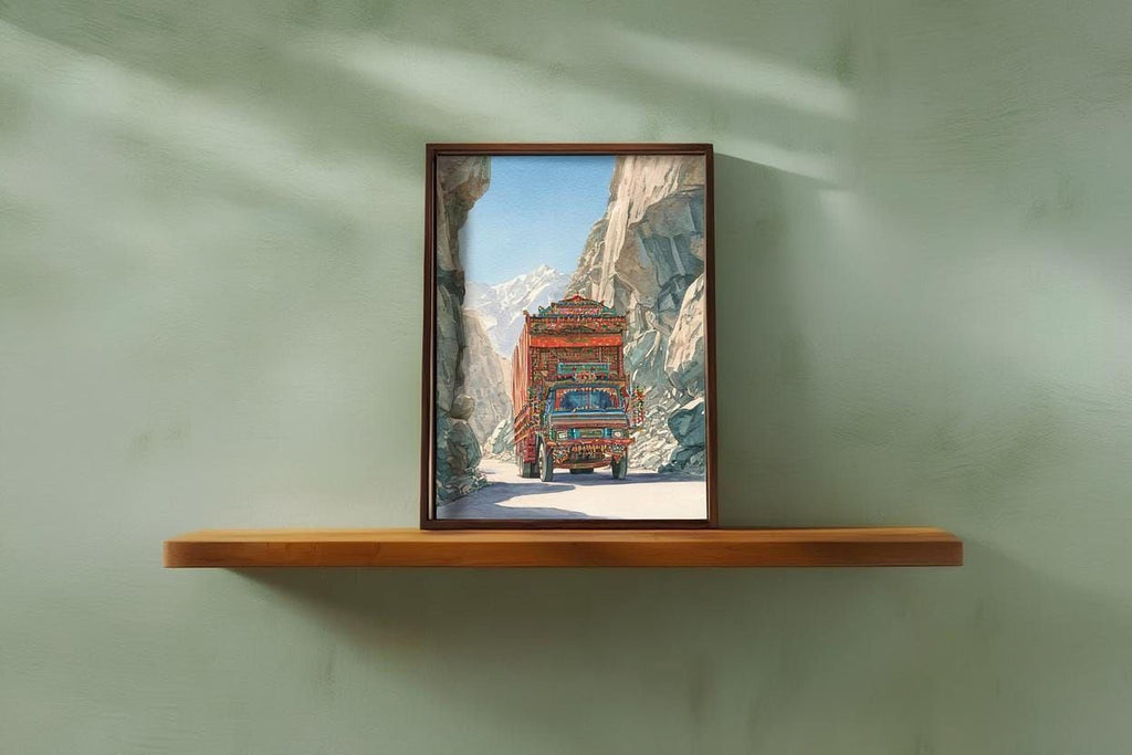 A framed photograph of a colorful truck driving through a mountainous landscape is displayed on a wooden shelf against a green wall.