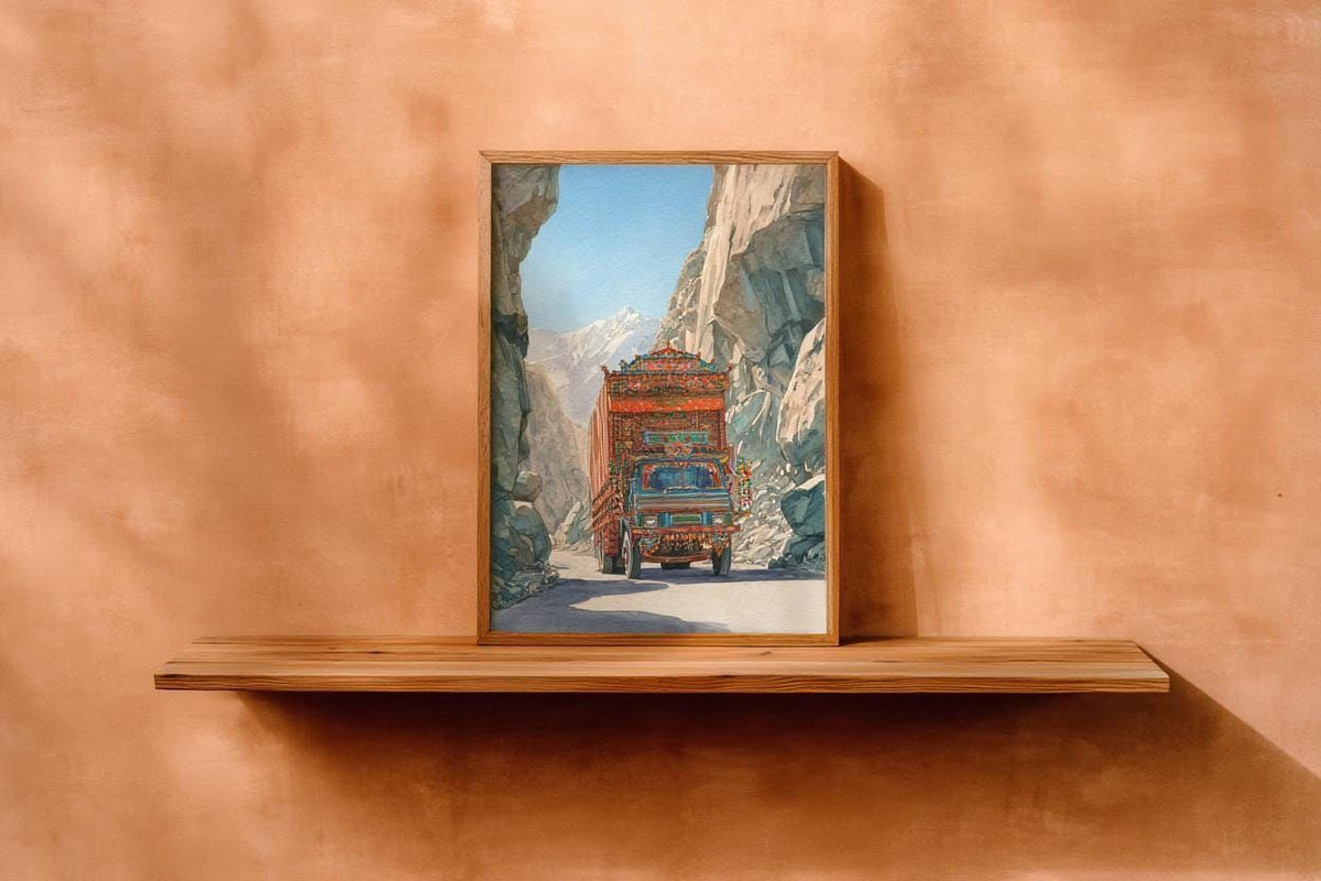 a wooden shelf displaying a framed painting of a colorful truck driving through a mountainous landscape.