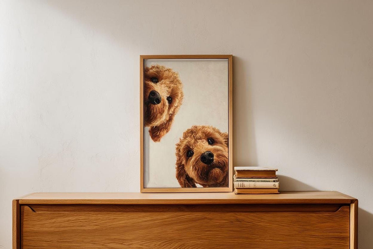 A framed painting of two brown dogs peeking out from behind a wooden shelf, with a stack of books below it.