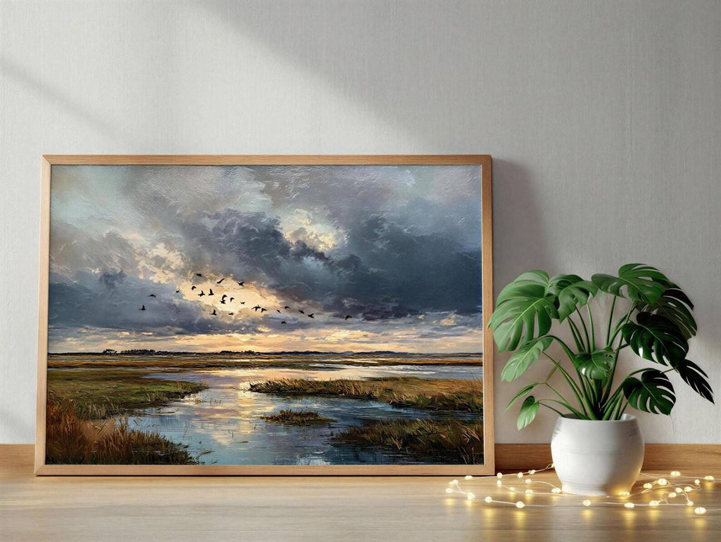 a framed painting of a serene landscape with a river, a flock of birds flying over the water, and a cloudy sky with a sunset. The painting is displayed on a wooden shelf next to a potted plant with white flowers.