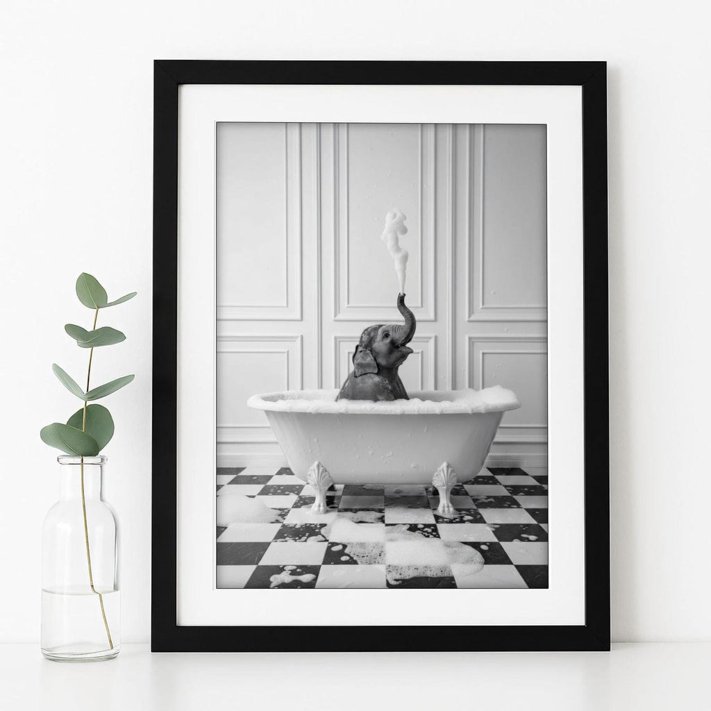 A framed black and white photograph of a baby elephant sitting in a bathtub, with a plant in a glass vase next to it.