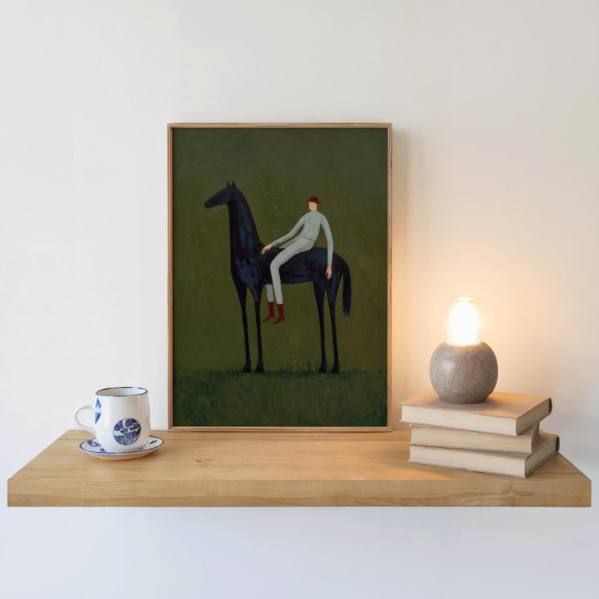 Boho equestrian decor on shelf, framed horse and rider wall art beside books and a warm lamp glow.