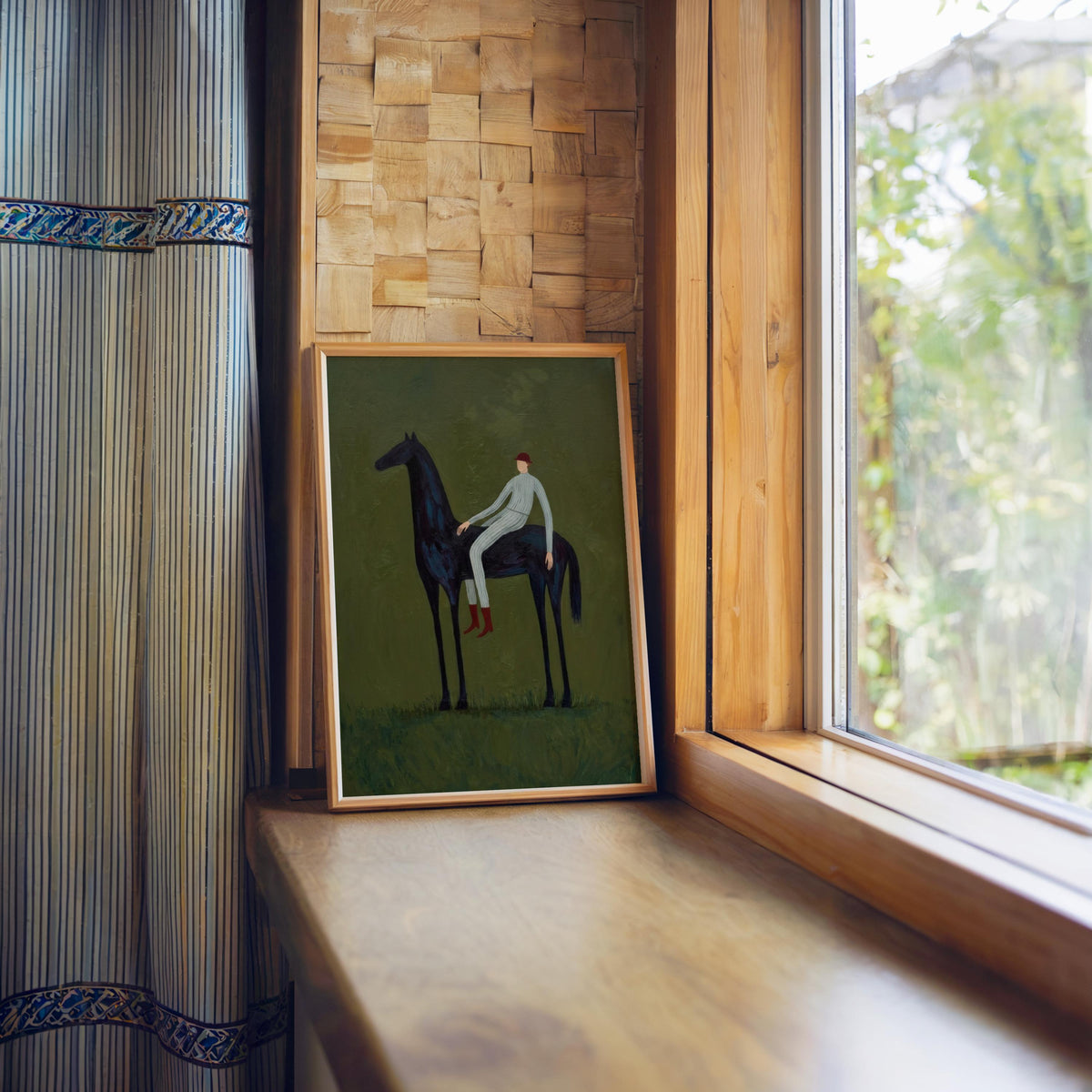 Vertical horse wall art in sunlit window nook, framed dark horse and rider on muted olive, warm wood frame.