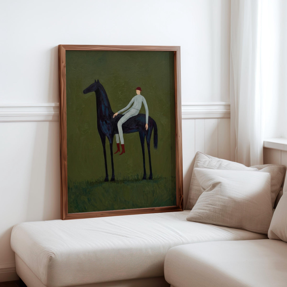 Framed vintage equestrian wall art displayed on living room sofa, slim wood frame, olive green tones.