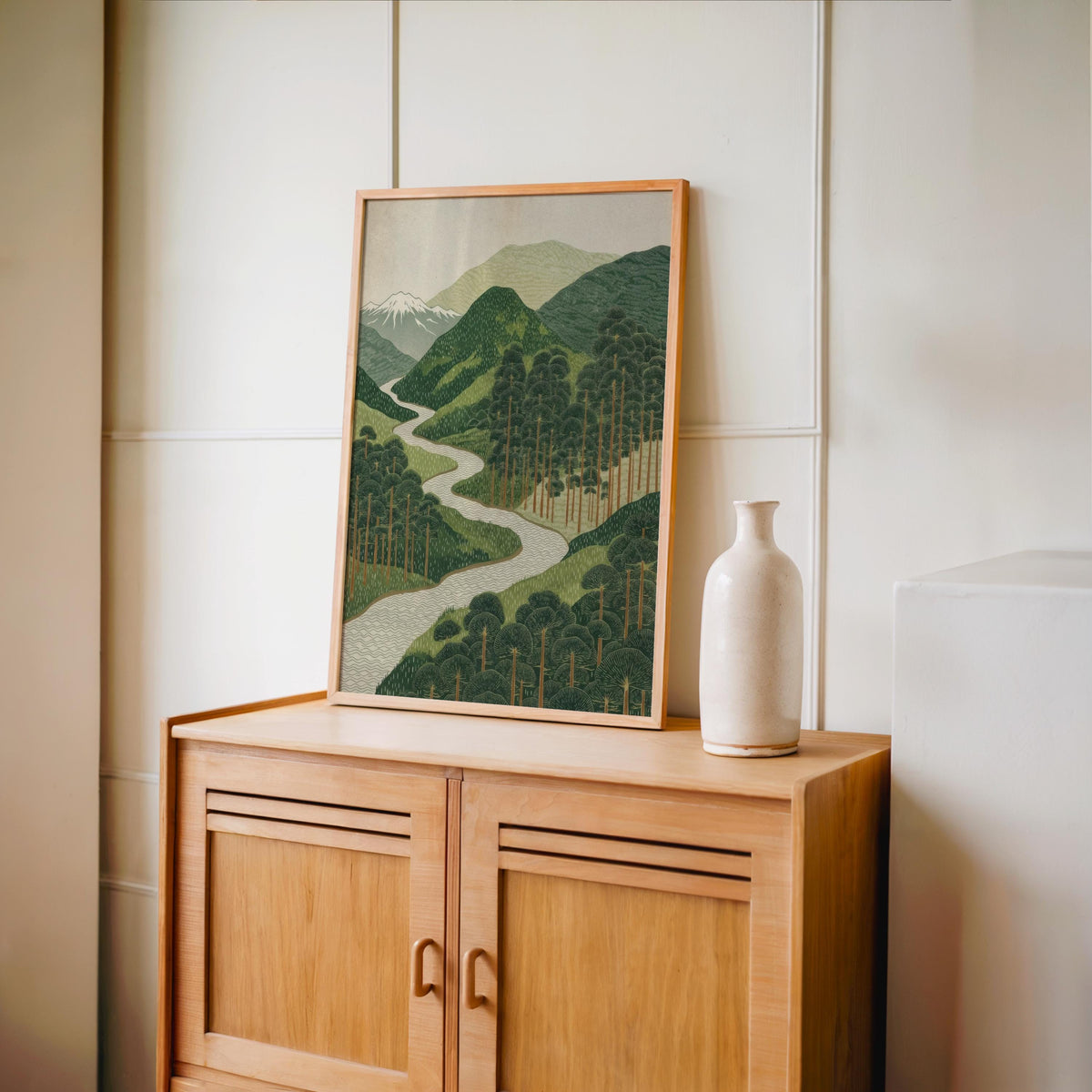 Slim frame on a wooden cabinet with ceramic vase, serene mountain art print in a minimalist setting