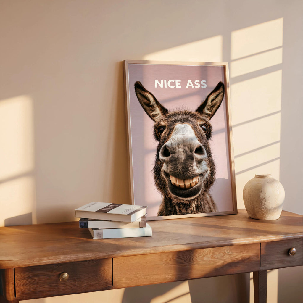 Blush pink funny donkey bathroom sign leaning on wood ledge, close crop of donkey grin, funny toilet wall art