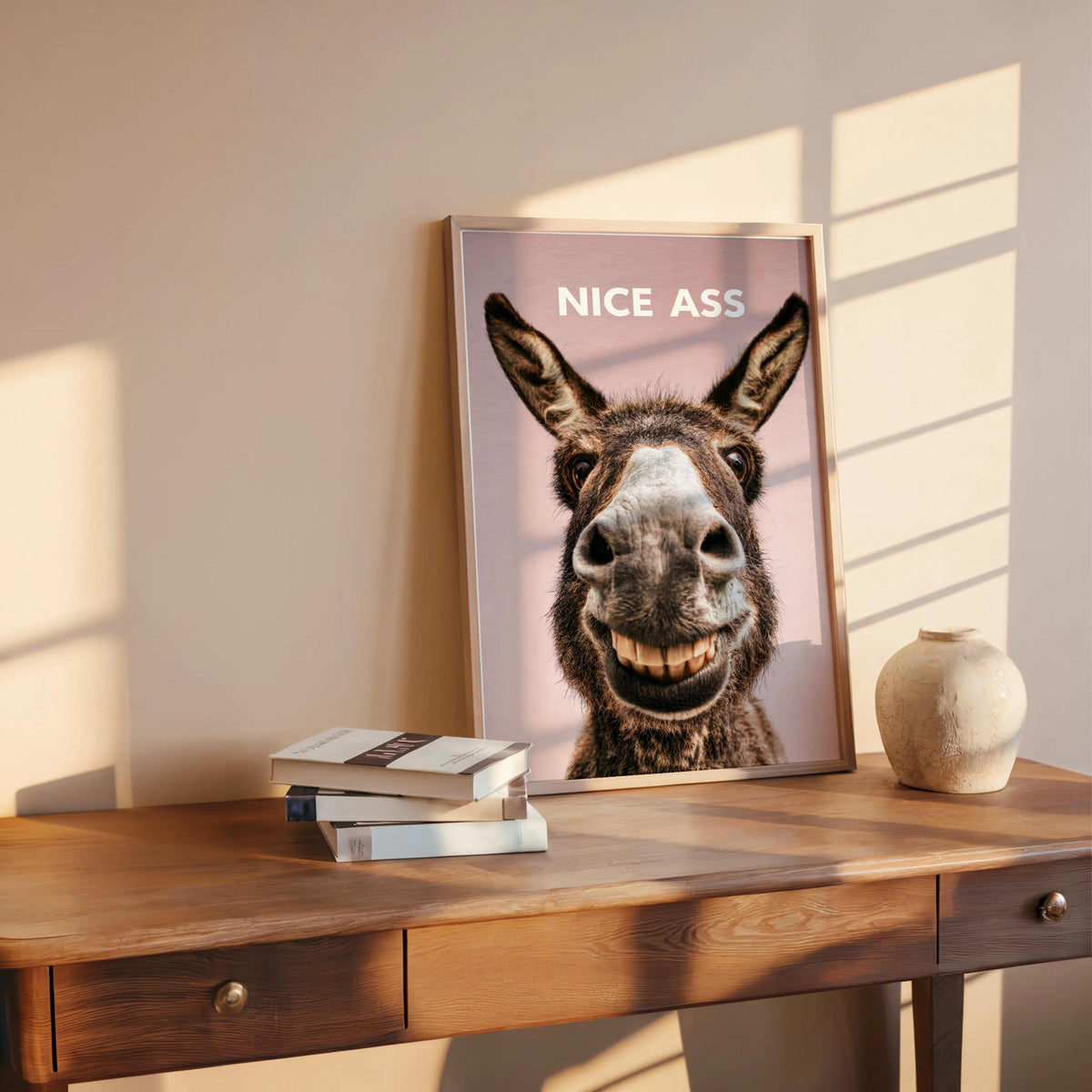 Blush pink funny donkey bathroom sign leaning on wood ledge, close crop of donkey grin, funny toilet wall art