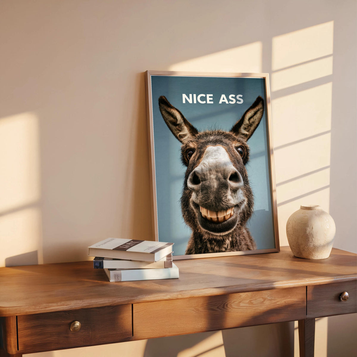Blue-gray backed funny donkey bathroom sign resting on console, stacked books and small vase beside frame