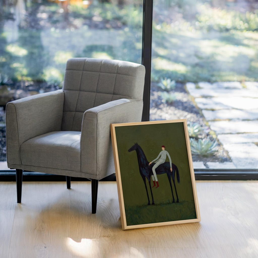 Green horse wall decor angled by bright window, framed horse and rider art placed near a gray armchair.