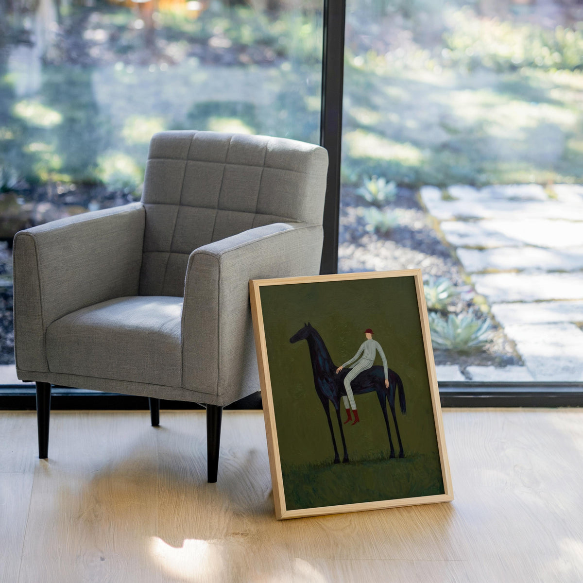 Green horse wall decor angled by bright window, framed horse and rider art placed near a gray armchair.