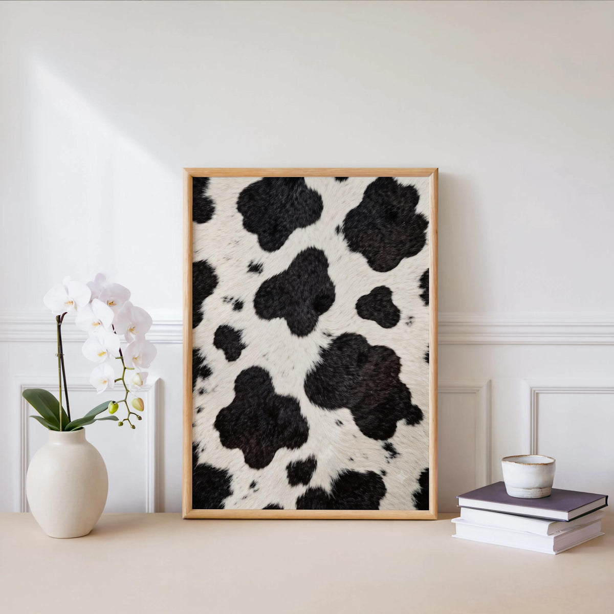 Black and white cow art on a white shelf, potted orchid and a stack of books for clean decor
