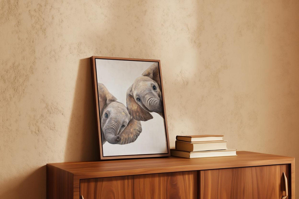 Framed baby elephant wall art leaned on wood dresser with books, neutral safari nursery decor and texture