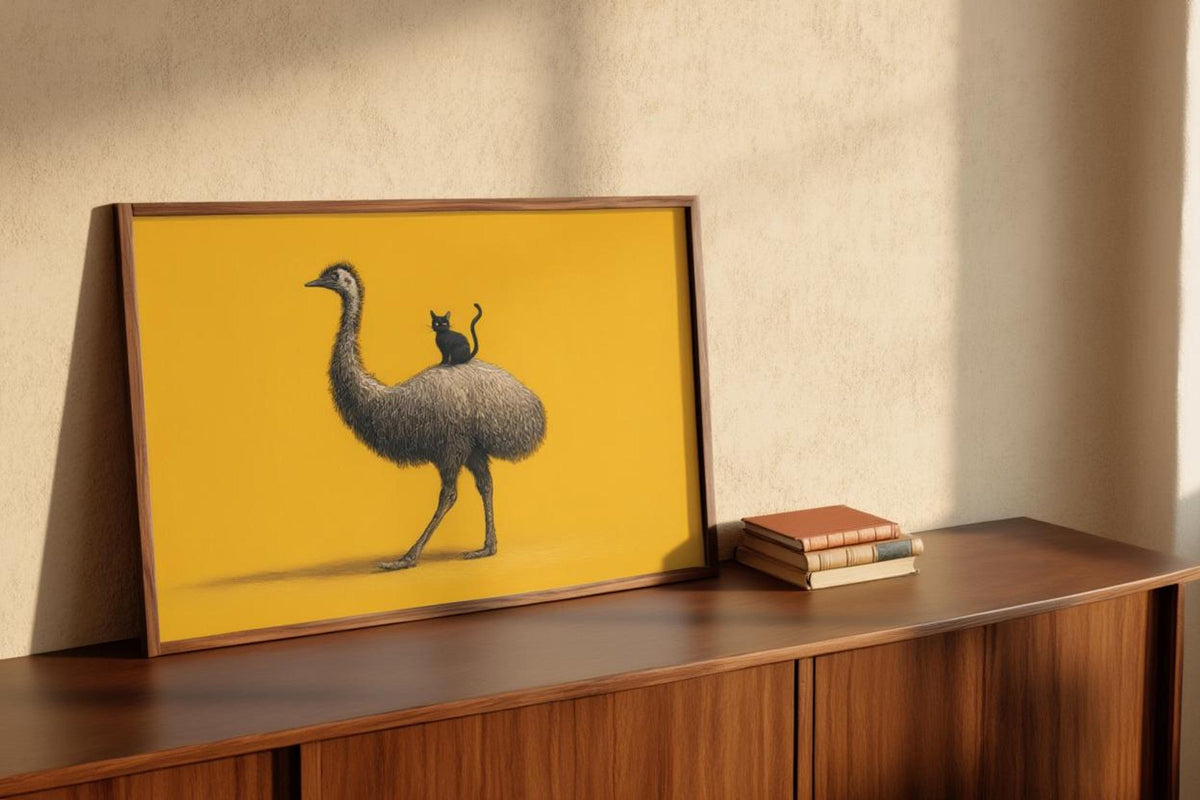 Framed emu print leaning on midcentury wooden sideboard, warm light highlights fine feather linework