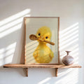 Framed yellow duckling kitchen wall art leaning on sunlit shelf, textured painterly duckling holding spoon.
