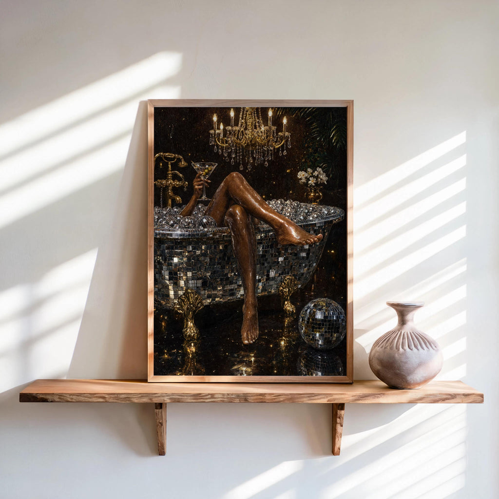 Framed disco ball bathtub art print leaning on a sunlit wooden shelf, black and gold sparkle, ceramic vase beside it