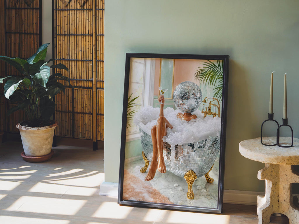 Disco ball woman wall art framed print propped on a pale green wall, potted plant and morning light