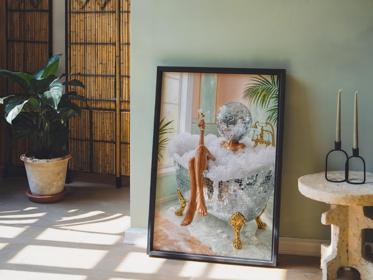 Disco ball woman wall art framed print propped on a pale green wall, potted plant and morning light