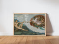 Framed creation of adam funny wall art print leaning against white wall, wood floor, cracked fresco texture