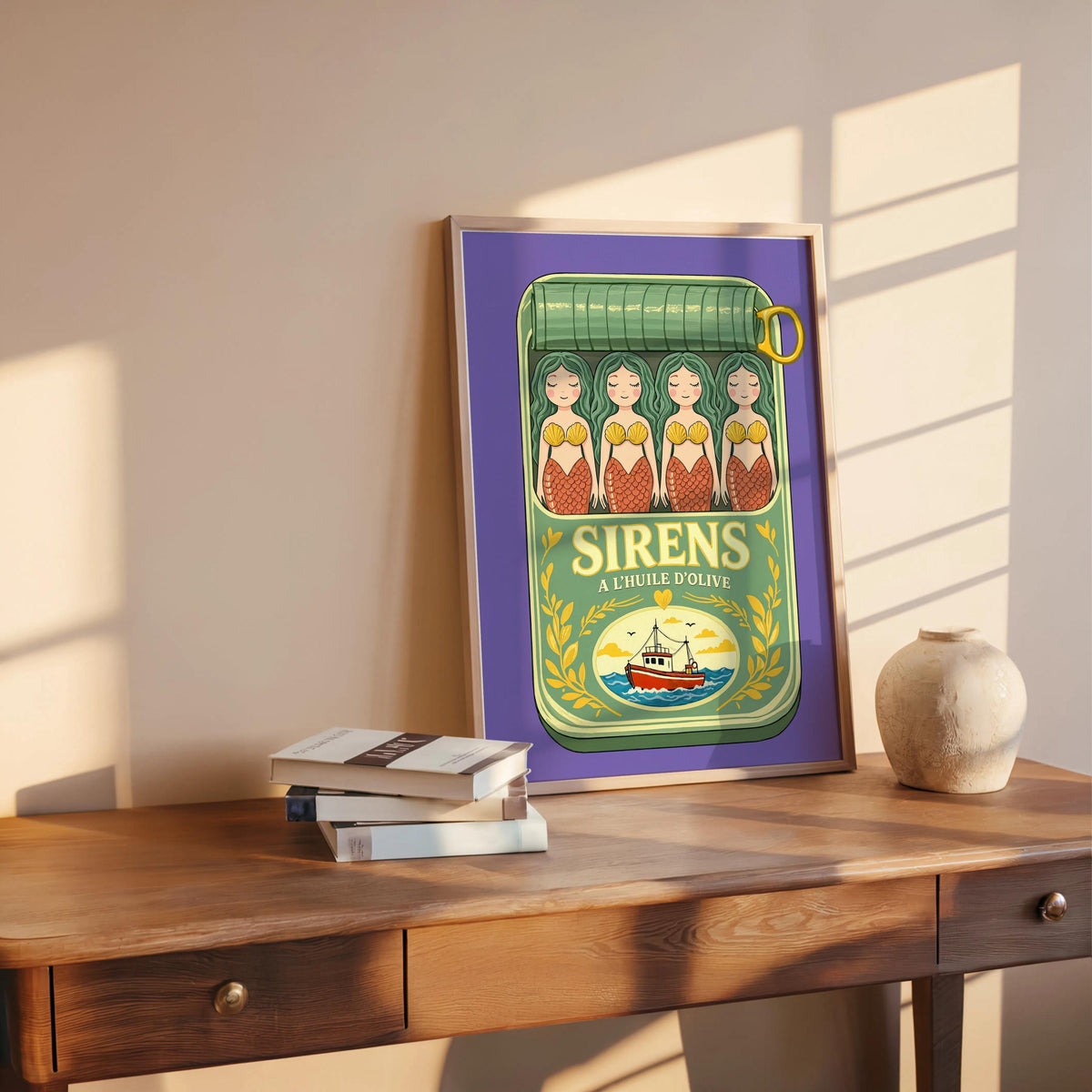 Purple-framed mermaid sardine tin art print leaning on wooden table, books and ceramic bowl, cozy vignette