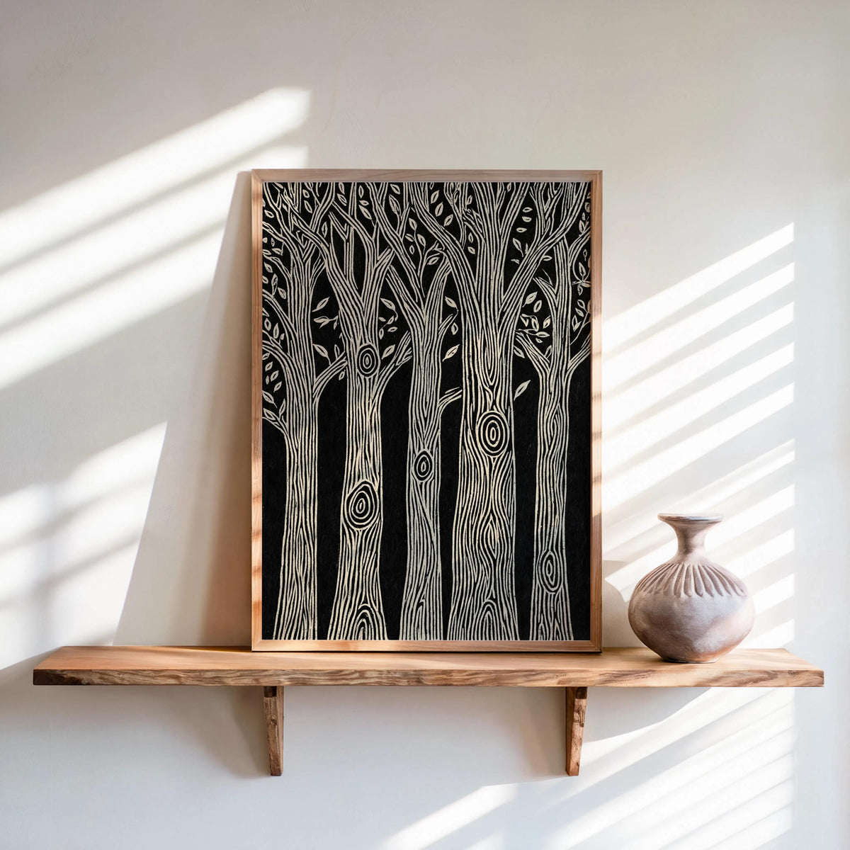 Black and white forest wall art leaning on a floating shelf, light wood frame, sunlit striped shadows, linocut forest print