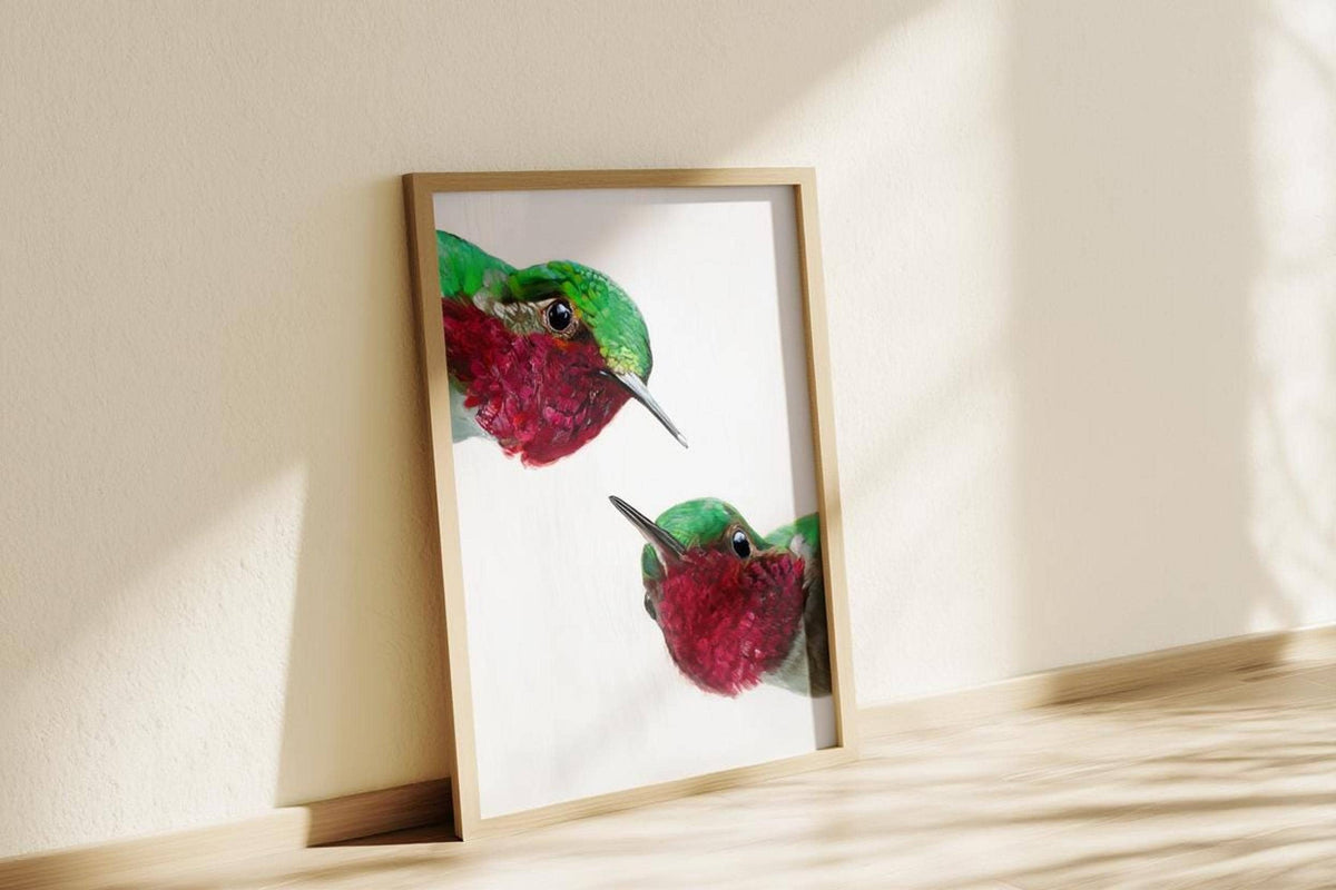Sunlit whimsical hummingbird wall art print leaning on warm cream wall, comical red and green birds, playful decor.