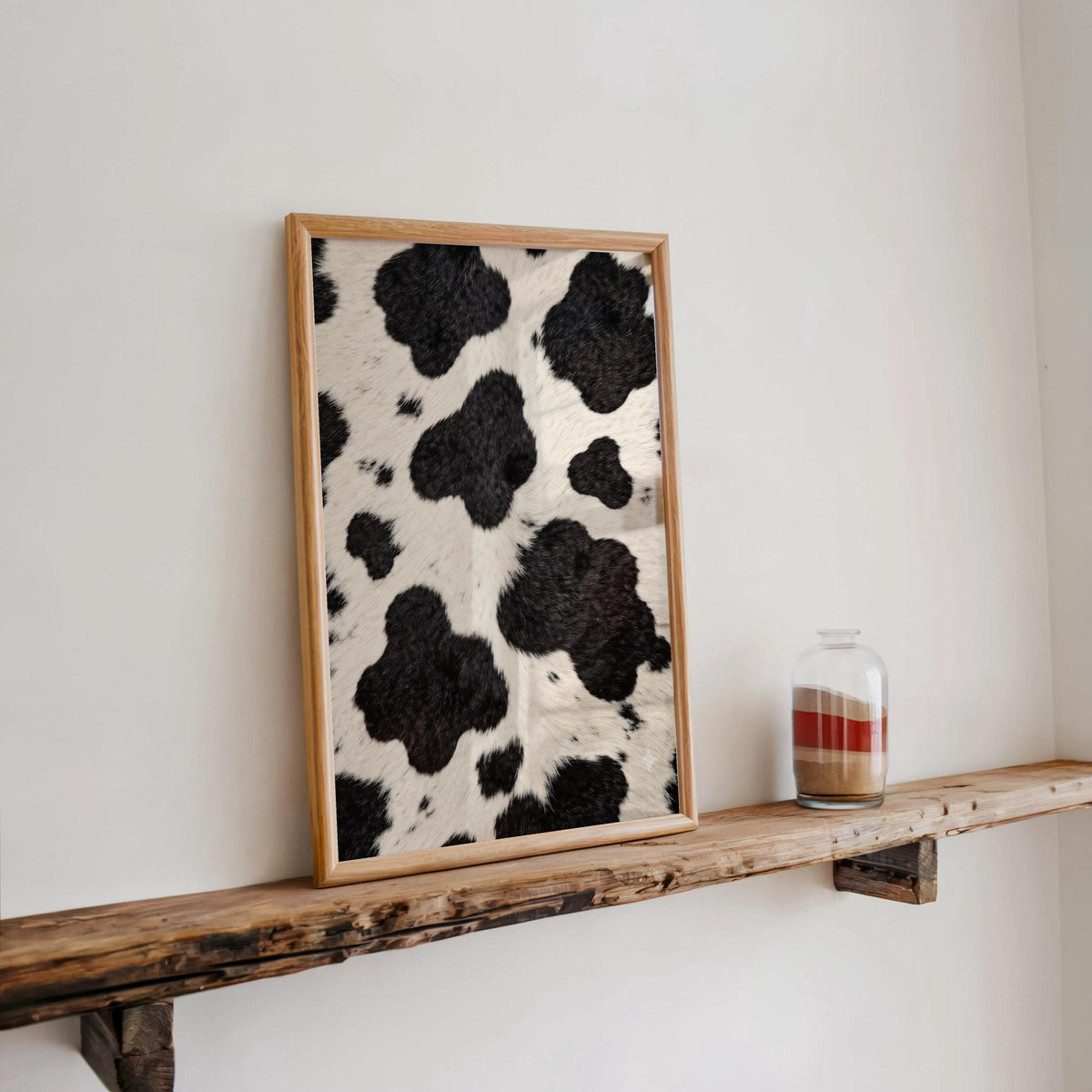Cow print poster leaning on a rustic shelf, small candle jar and warm, cozy farmhouse lighting