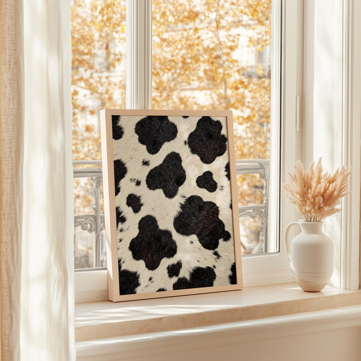 Cow print poster on a sunny windowsill, golden autumn foliage outside, neutral vase beside it