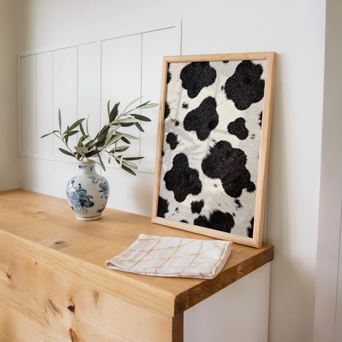 Cowhide print leaning on a wooden desk, ceramic vase with branches and an open notebook nearby