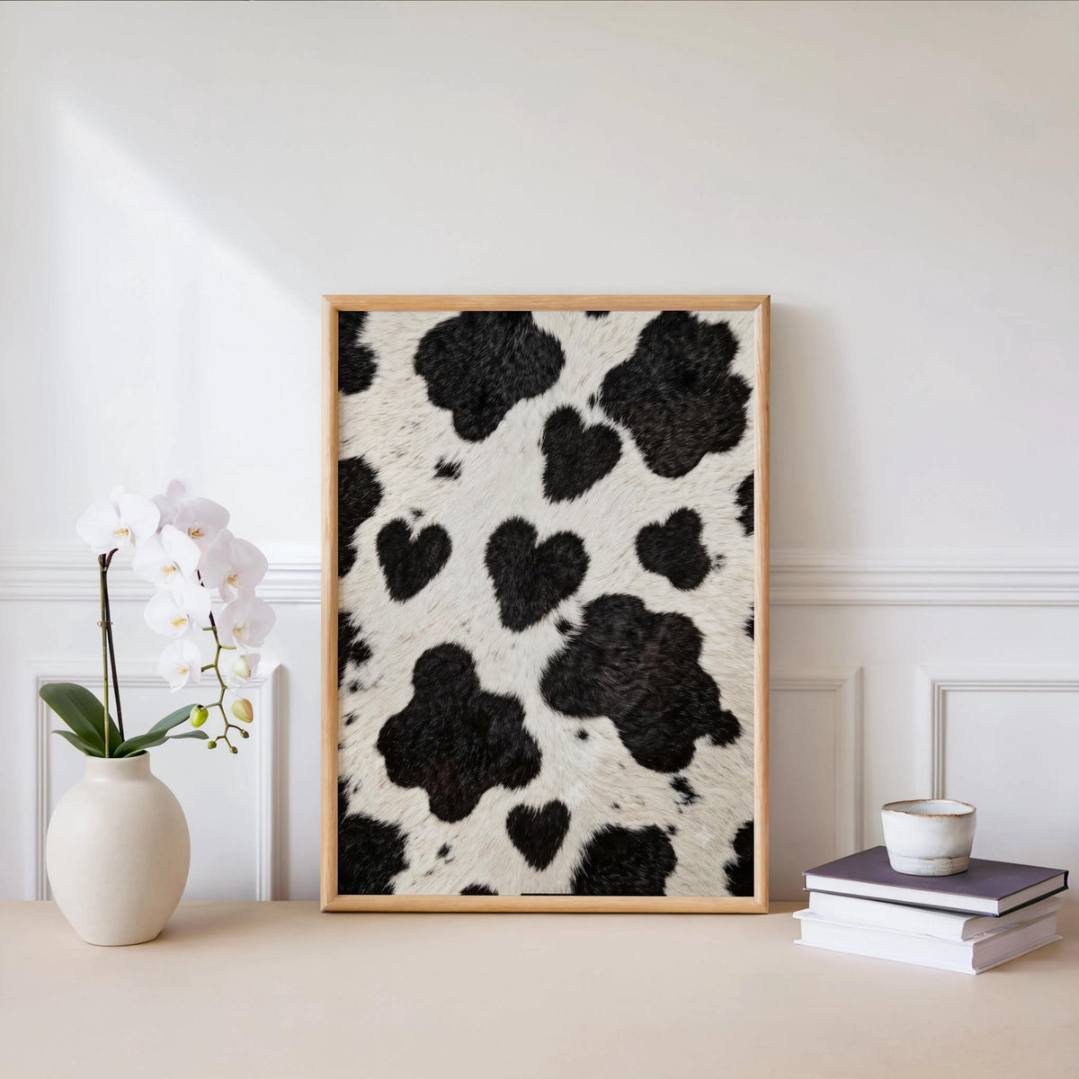 Heart cow print wall art leaning on a white ledge, orchid and candle accents, minimalist farmhouse look