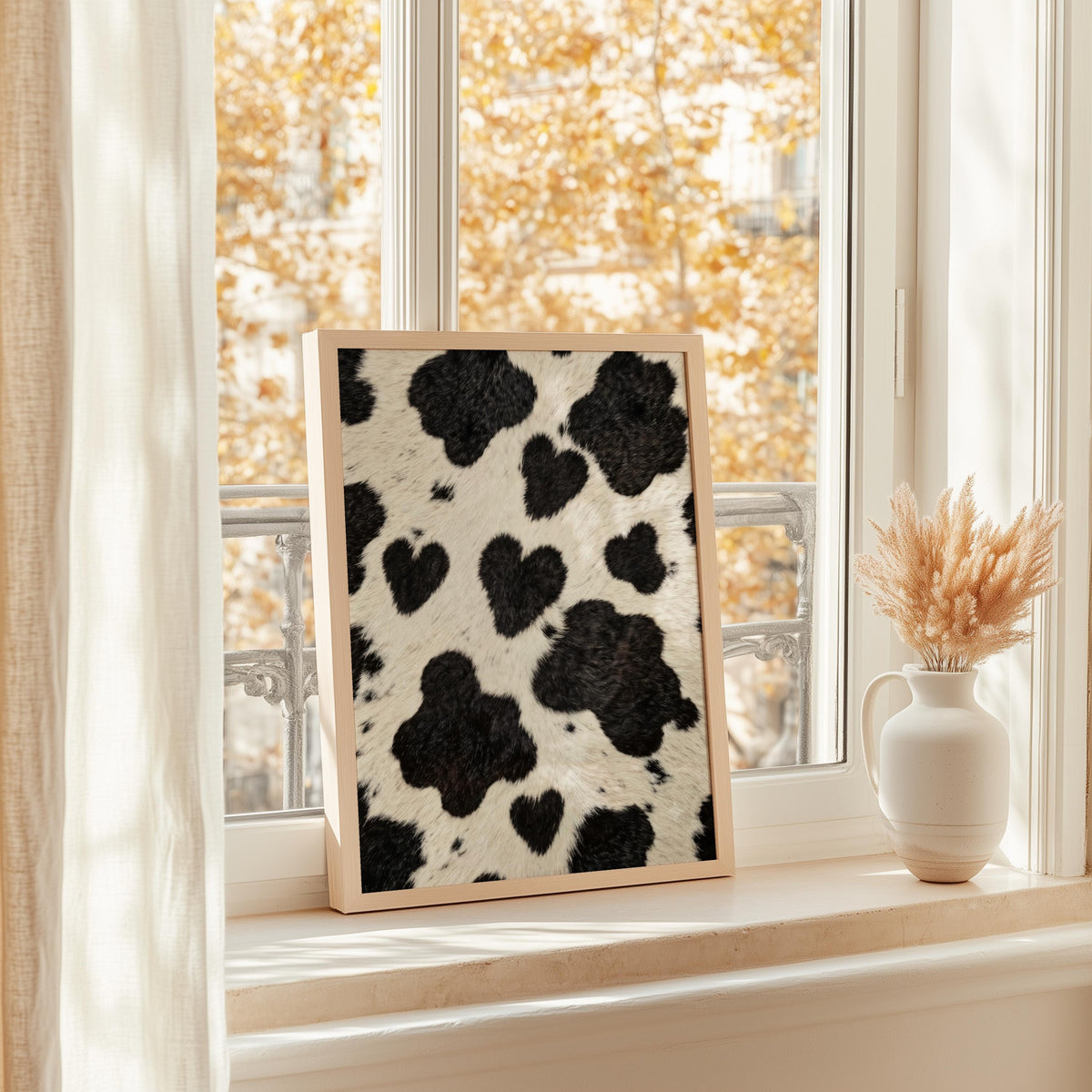 Heart cow print wall art on a bright windowsill, dried grass vase, golden autumn trees outside
